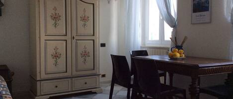 Un coin repas comprenant une table en bois, des chaises, un buffet orné de motifs floraux et une fenêtre avec des rideaux.