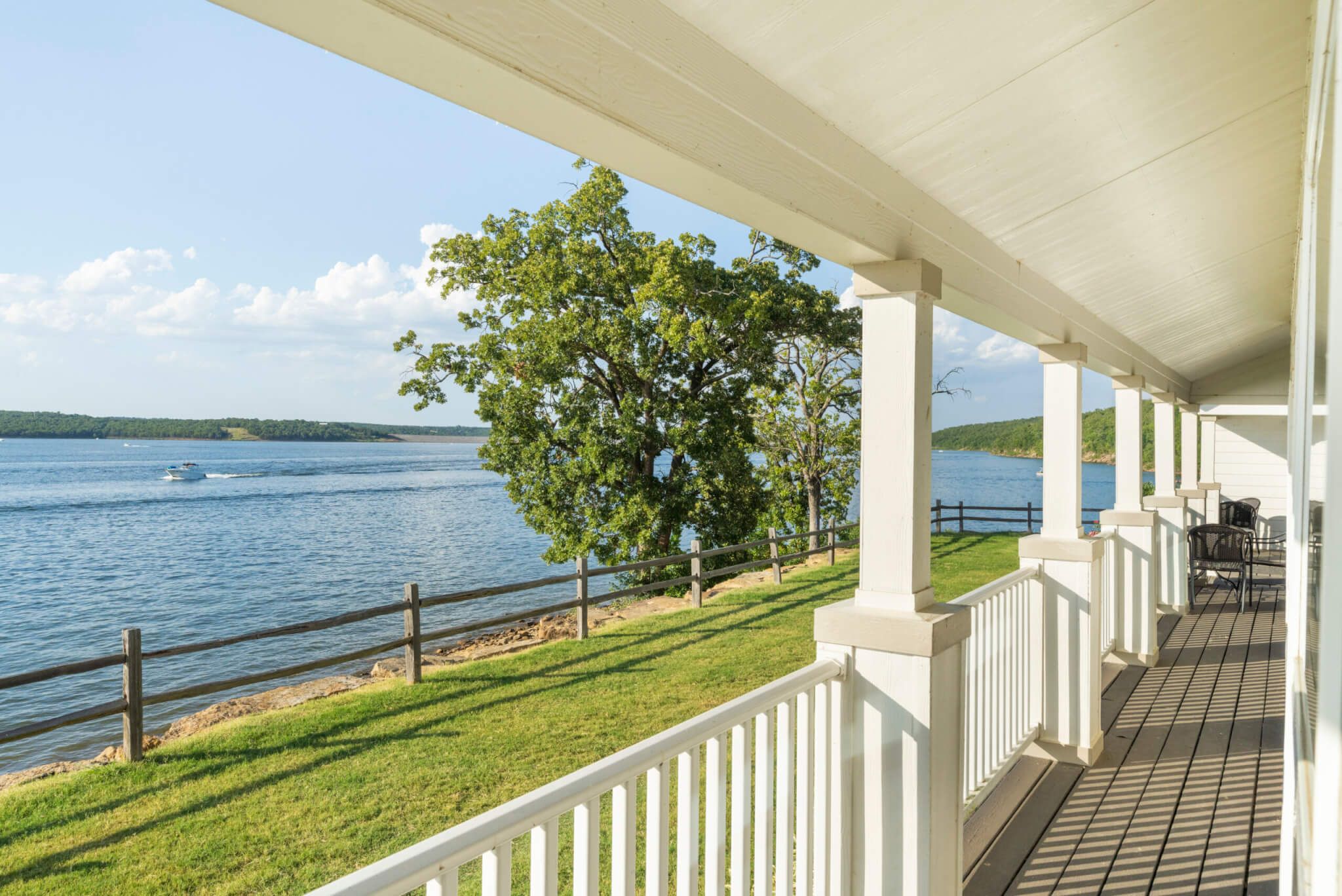 A covered porch with a view of a lake and a tree.