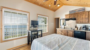 A bedroom with a bed, a desk, and a television. There is a kitchen area with cabinets and a refrigerator. - Shoreside at CrossTimbers Marina (Sperry)