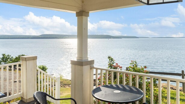 A covered outdoor area with a view of a large body of water, a white railing, and a round table. - Shoreside at CrossTimbers Marina (Sperry)