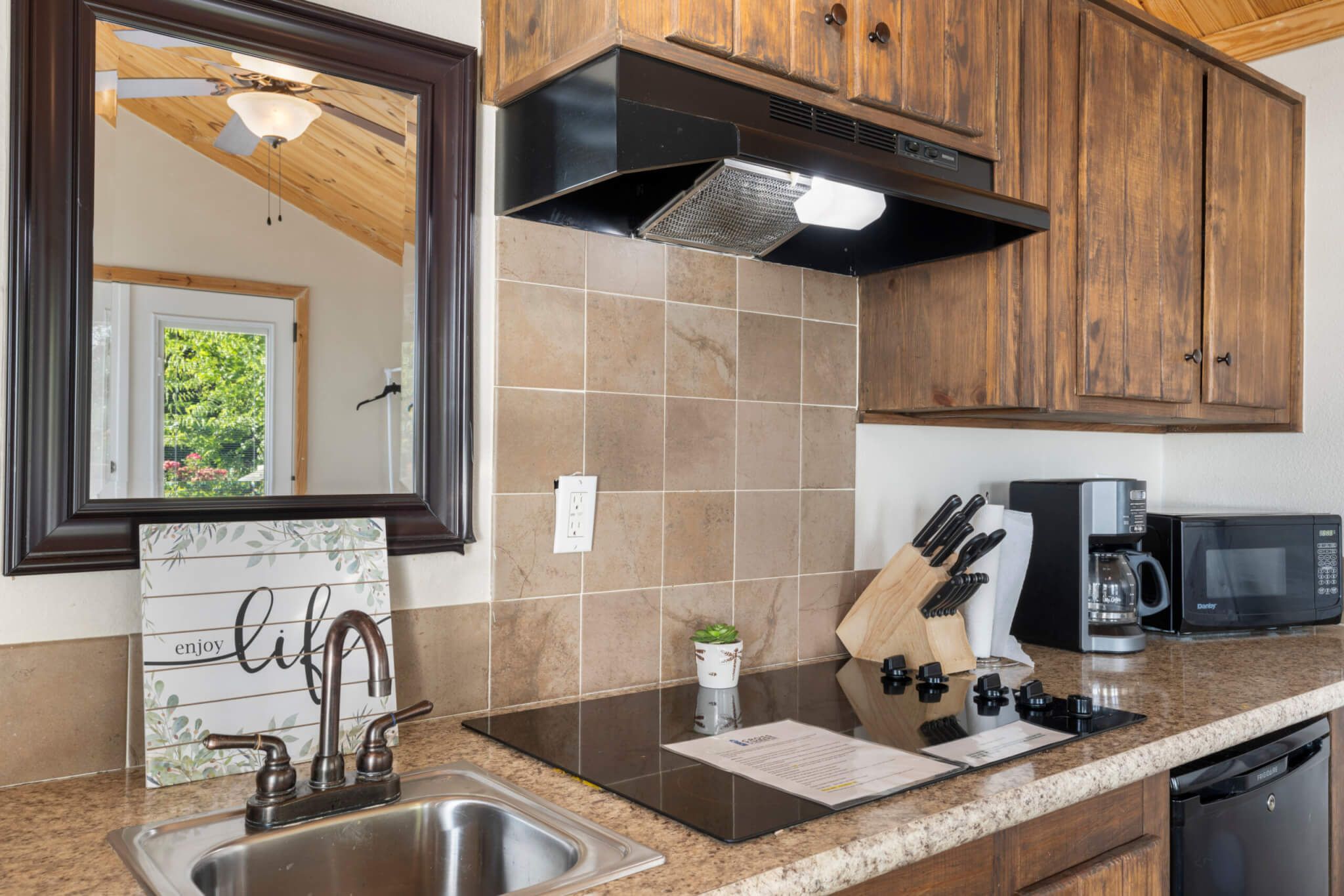 A kitchen with a stainless steel sink, wooden cabinets, a microwave, and a coffee maker.