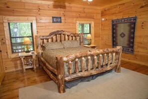 Camera da letto in una baita di legno, con un letto rustico, due lampade da comodino, una finestra con persiane e un tappeto decorativo.