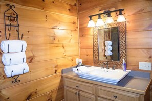 Bagno di una baita in legno con lavandino, specchio e porta asciugamani.