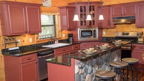 A kitchen with red cabinets, a granite countertop, a stone island, and a coffee sign. - Hillbilly Hotel, Great Resort, Great Game Room (Sevierville)