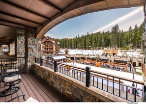A wooden deck with stone walls, overlooking a ski resort with buildings and trees.