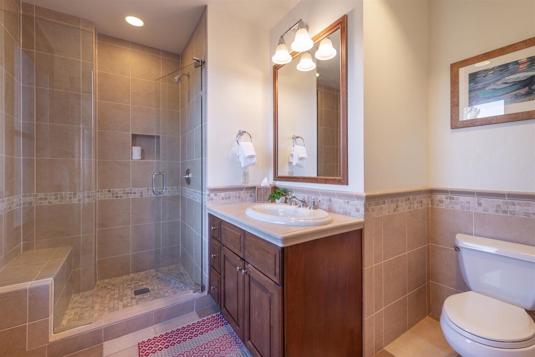 A bathroom with a glass-enclosed shower, a sink with a mirror, and a toilet.