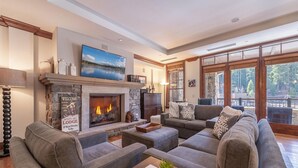 A spacious living room with a stone fireplace, comfortable seating, and a large window offering a scenic view. - Luxury 3BD Village at Northstar Residence - Great Bear Lodge 303 (Truckee)