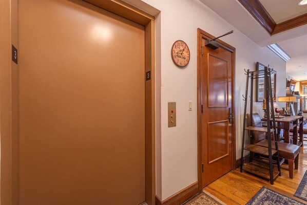 A hallway with a closed door, a wall clock, and a coat rack.
