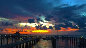 Une jetée s’avançant dans l’eau, avec un coucher de soleil en arrière-plan.