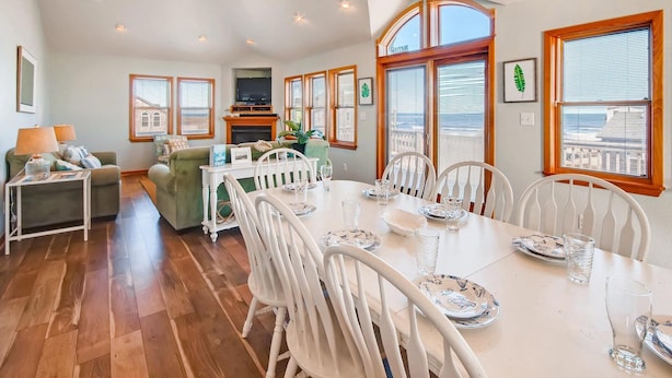 A dining area with a white table set for six, surrounded by white chairs. - Oceanview Dog Friendly Home w/ Private Pool, Hot Tub, and Beach Access Nearby (Rodanthe)