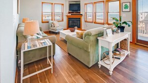 A living room with a fireplace, a television, and a view of the outside. - Oceanview Dog Friendly Home w/ Private Pool, Hot Tub, and Beach Access Nearby (Rodanthe)