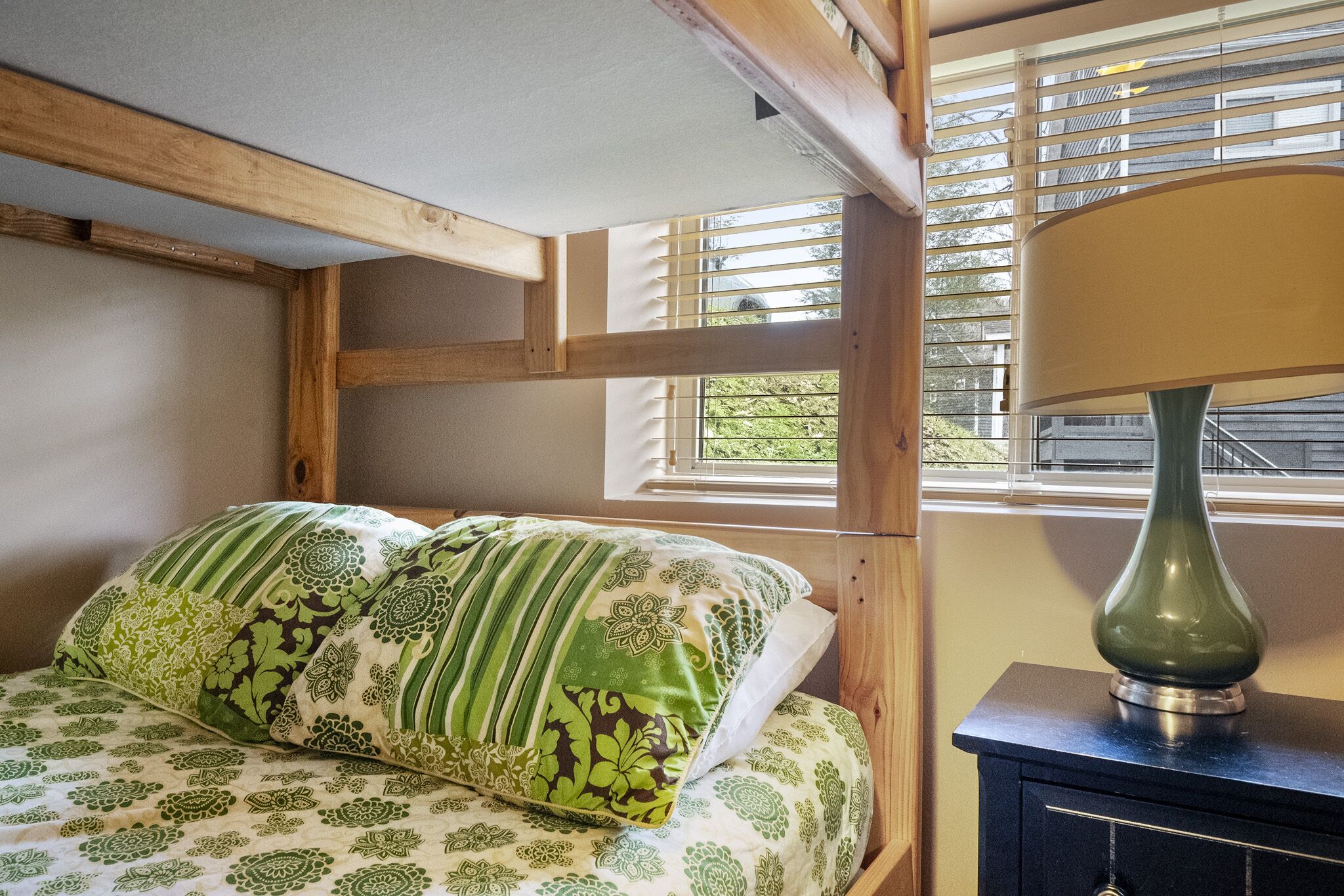 A bedroom with a bed, pillows, a lamp, and a window with blinds.