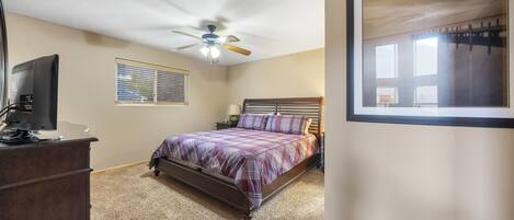 A bedroom with a bed, a ceiling fan, a dresser, a window with blinds, and a framed picture on the wall.