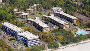 Un hotel frente al mar con varias construcciones, una playa y una zona de piscina.