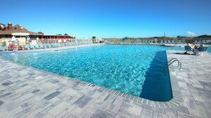 Piscina con agua azul cristalina, rodeada de sillas de descanso y un solárium con baldosas.