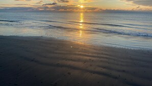 Una playa con el sol reflejándose en el agua al atardecer.