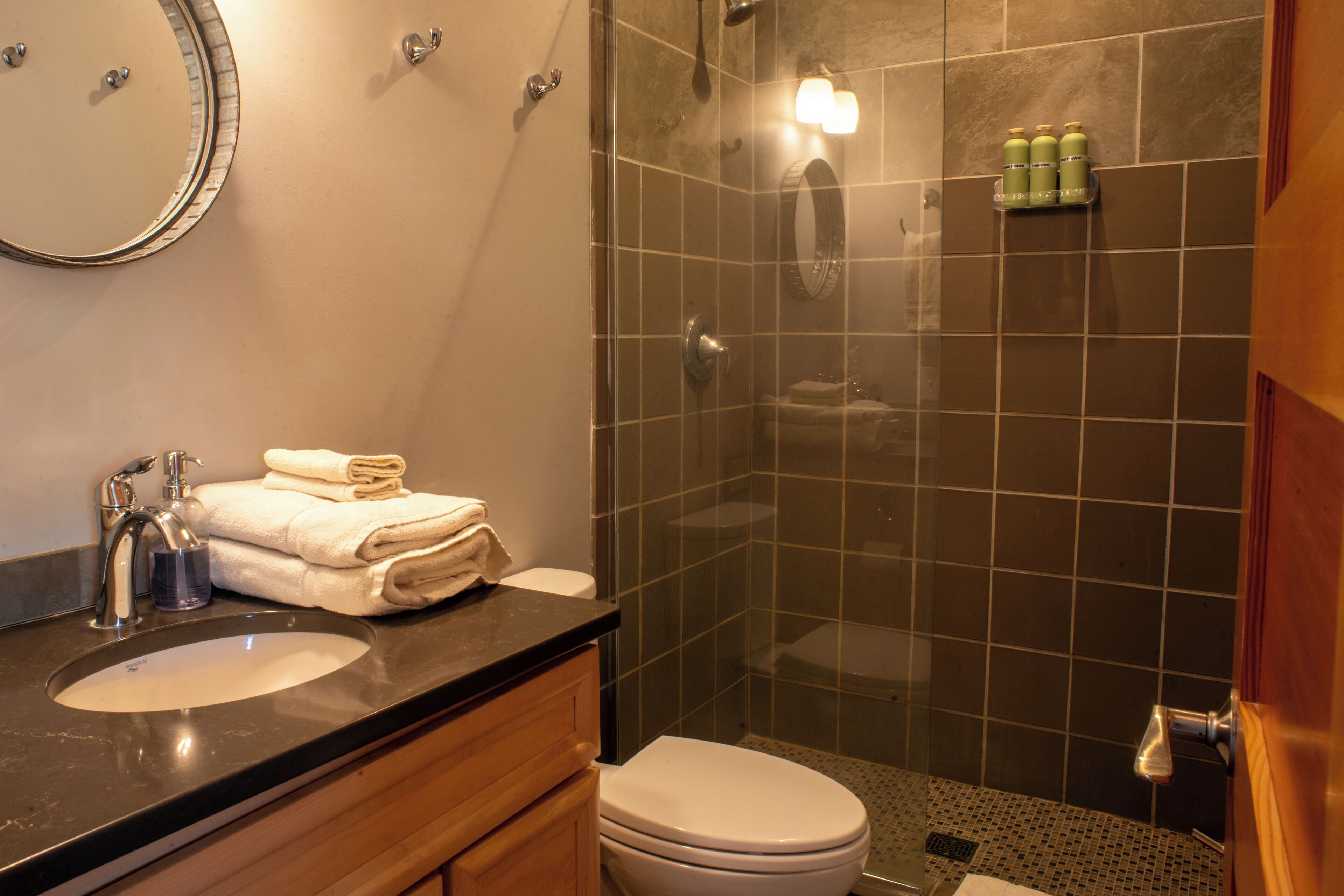 A bathroom with a sink, mirror, and a glass-enclosed shower stall.
