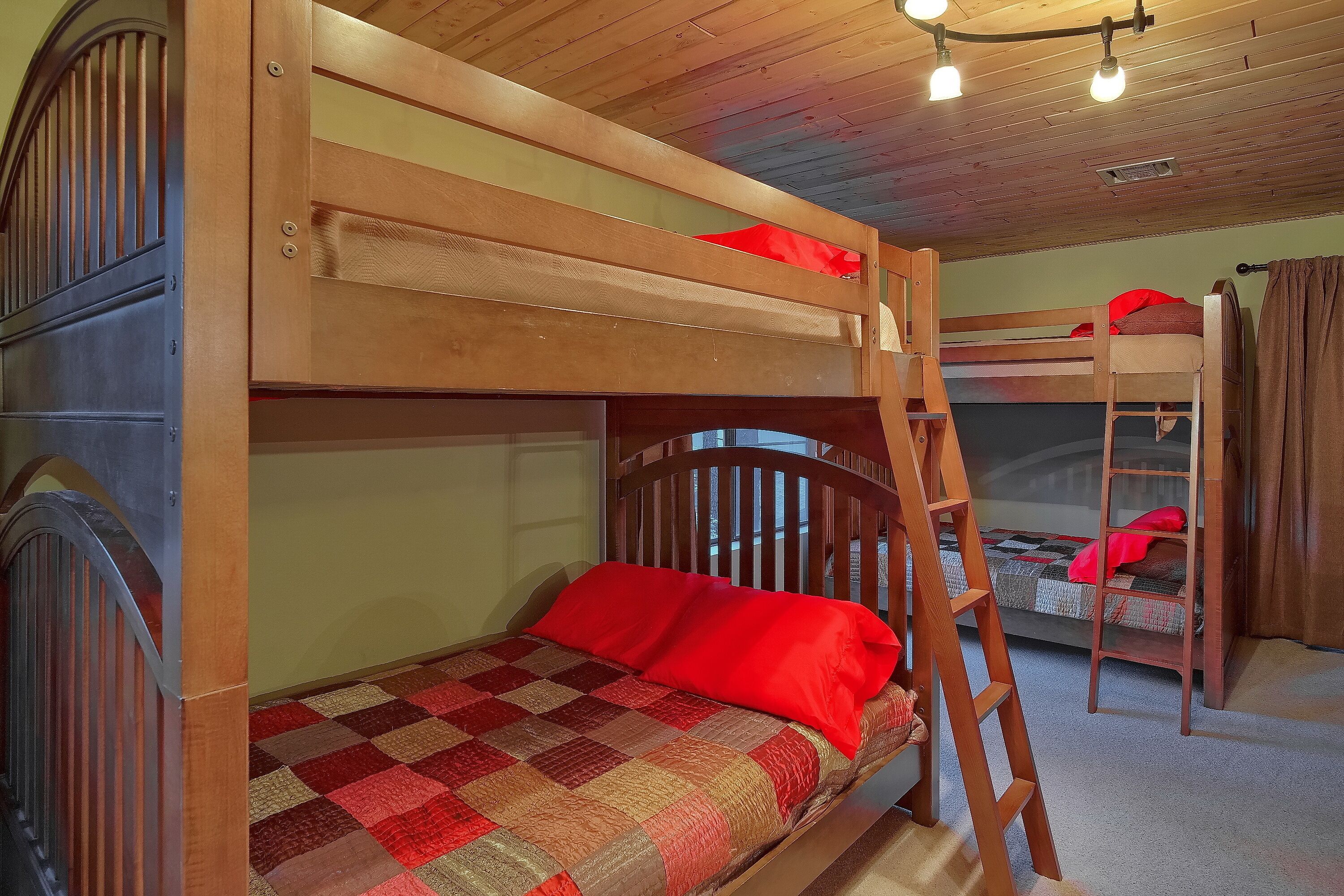 Habitación con literas, una escalera, colcha de cuadros y techo de madera.