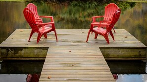 Una banchina di legno con due sedie rosse rivolte verso un lago tranquillo, circondata da autunno e una collina boscosa.