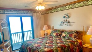 A bedroom with a bed, two bedside lamps, a ceiling fan, a window with curtains, and a decorative wall piece. - Beautiful Oceanfront Condo On 4th Floor - Steps From The Beach. Linens Incl. !!! (Surfside Beach)
