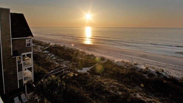 A beachfront property with a two-story building, a wooden deck, and a view of the ocean at sunset. - Beautiful Oceanfront Condo On 4th Floor - Steps From The Beach. Linens Incl. !!! (Surfside Beach)