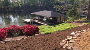 A lakeside cabin with a dock, surrounded by lush greenery and a well-maintained garden. - Amazing Views at Dragonfly! HOT TUB! Kayaks, BOUNCER w Slide, SUP's, Fire Pit!  (Bracey)