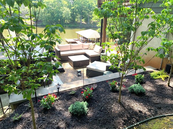 Relax on the L-shaped sofa set in this serene outdoor space, surrounded by lush greenery and a tranquil body of water.