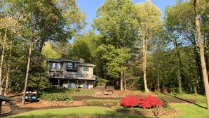 A two-story house with a balcony, surrounded by a well-maintained garden and a pond. - Amazing Views at Dragonfly! HOT TUB! Kayaks, BOUNCER w Slide, SUP's, Fire Pit!  (Bracey)
