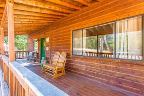 Una cabaña de madera con un porche, dos sillas Adirondack y un banco.