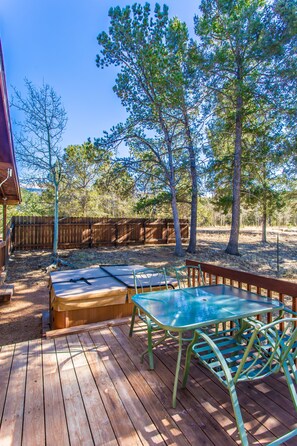 A wooden deck with a glass table and chairs, surrounded by trees and a wooden fence.