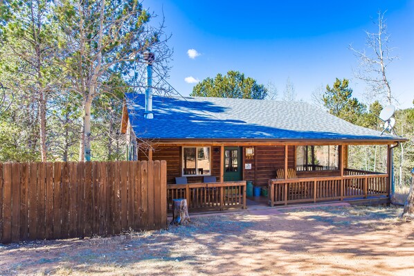 A wooden cabin with a porch, surrounded by trees.