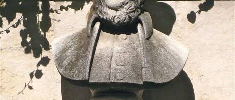 A stone bust sculpture mounted on a pedestal, set against a stone wall with ivy.