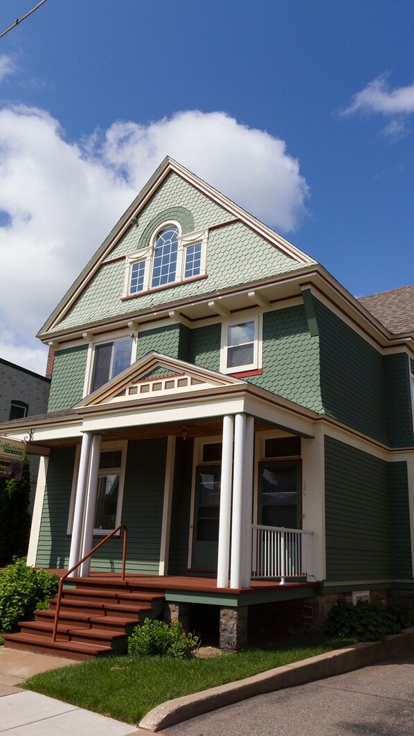A two-story house with a green roof, white trim, and a front porch with steps leading to a door. - Step Out the Door: Walk to the Best Dining and Breweries, 2 bikes included (Marquette)