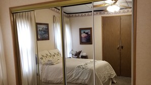 A bedroom with a large mirror, a bed with a floral bedspread, a nightstand with a lamp, and two framed pictures on the wall. - Beach House in Rehoboth Beach, DE (Rehoboth Beach)