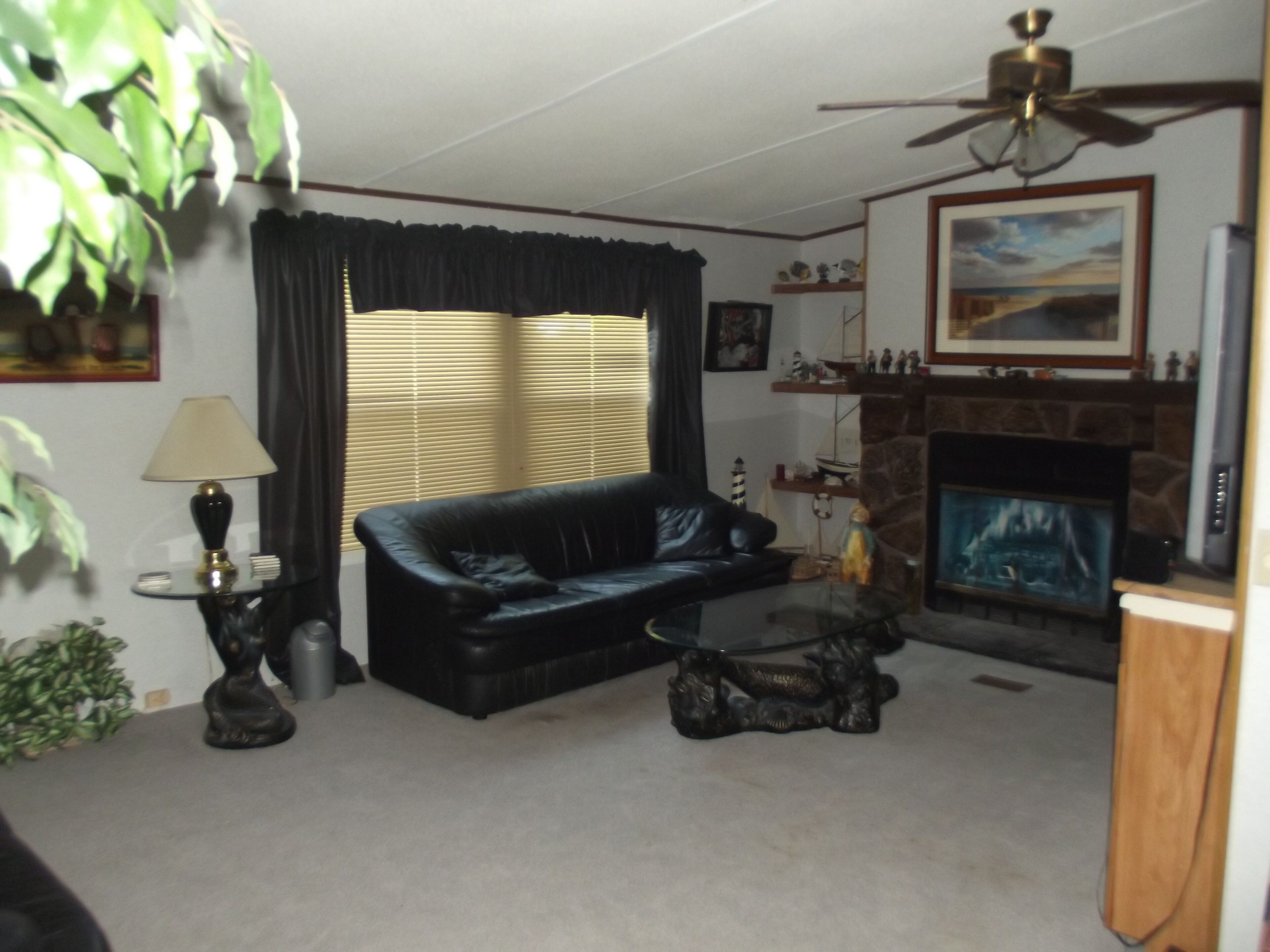A living room with a black leather sofa, a glass coffee table, a fireplace, and a ceiling fan.
