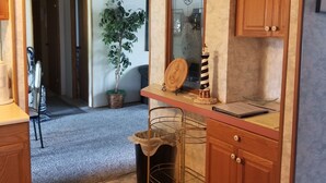 A kitchen with wooden cabinets, a countertop, a potted plant, a small island with a sink, and a trash can. - Beach House in Rehoboth Beach, DE (Rehoboth Beach)