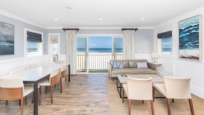 Een ruime woonkamer met balkon en uitzicht op zee, een eetgedeelte met een marmeren tafel en een gezellige zithoek met een bank en stoelen.