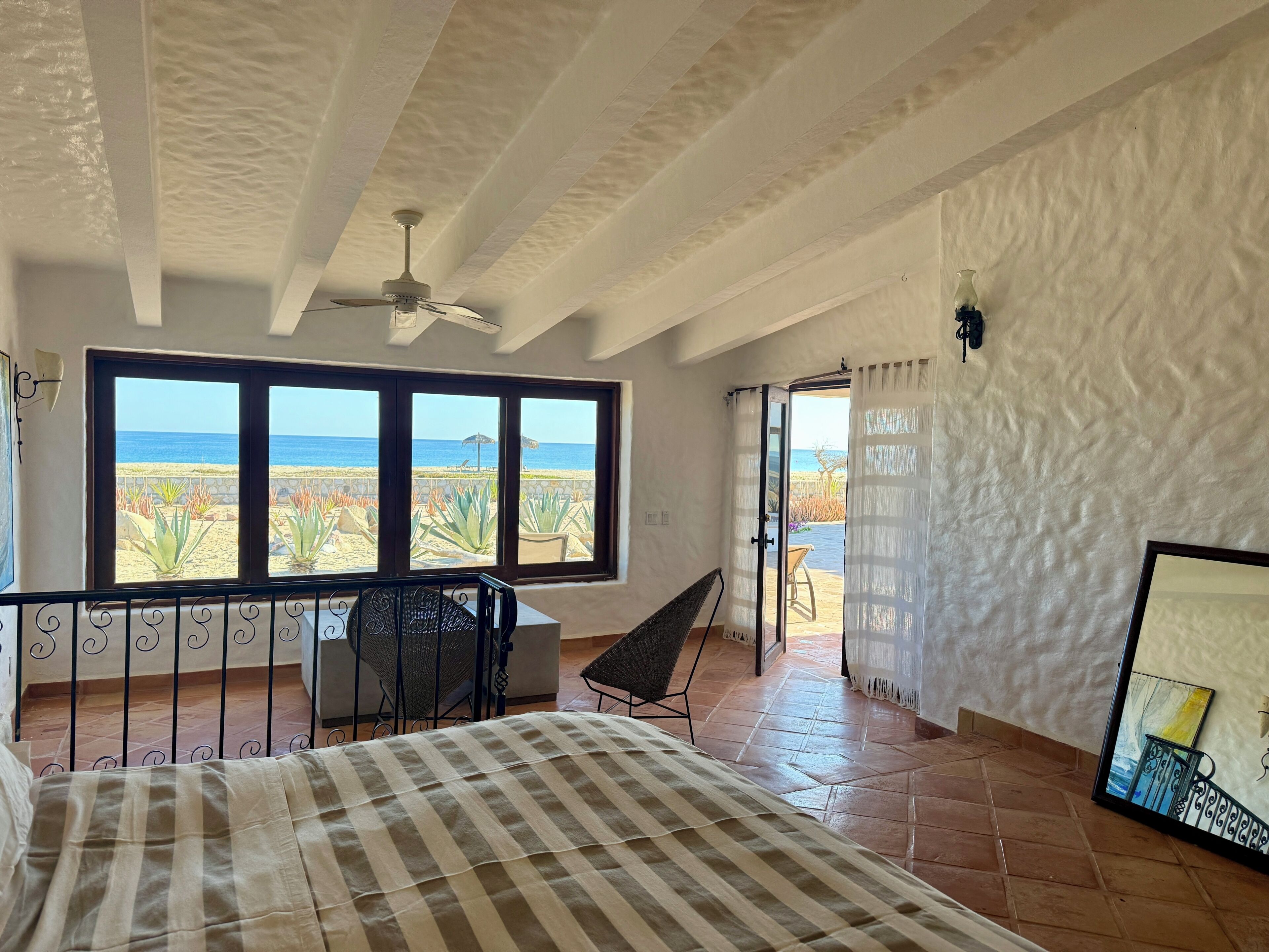 Een slaapkamer met een groot raam, een bed, een plafondventilator en uitzicht op het strand.