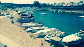 Una marina con barcos amarrados a la orilla, una playa de arena y un puente al fondo.