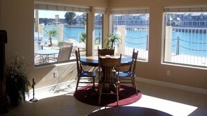 Comedor con mesa redonda y sillas, ventanas amplias con vista a una piscina y edificios, y un ventilador de techo.