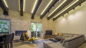 A modern living room with a stone wall, a grey sofa, a yellow chair, and a flat-screen TV. - PLATINUM RATED LUXURY CONDO IN VAIL VILLAGE WITH AC AND SKI LOCKER NEXT TO LIFT (Vail)
