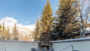 A pool with a stone fireplace, lounge chairs, and a view of trees. - PLATINUM RATED LUXURY CONDO IN VAIL VILLAGE WITH AC AND SKI LOCKER NEXT TO LIFT (Vail)