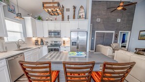 A modern kitchen with white cabinets, stainless steel appliances, and a central island with chairs. - Beach Front Home, Huge Deck, Sleeps 12 (Crystal Beach)