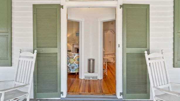 Une porte avec des volets verts ouverts, donnant sur une pièce où se trouvent un tapis à motifs, une poubelle et un meuble.