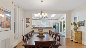 Un coin repas comprenant une table en bois, des chaises, un lustre et un meuble contenant des objets décoratifs.