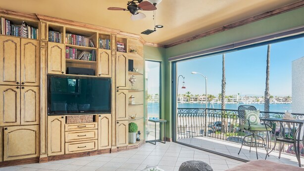 Un salón espacioso con televisor grande, muebles de madera y un balcón con vista al mar.