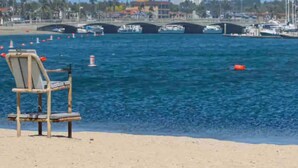 Una silla de playa sobre la arena, con vista a un puerto deportivo y montañas al fondo.