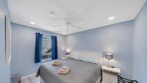 Een slaapkamer met een bed, twee bedlampen, een plafondventilator en een raam met gordijnen.