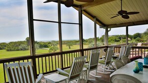 Un espace extérieur abrité, offrant une vue sur un paysage verdoyant, avec des fauteuils à bascule blancs et une table agrémentée d’objets décoratifs.