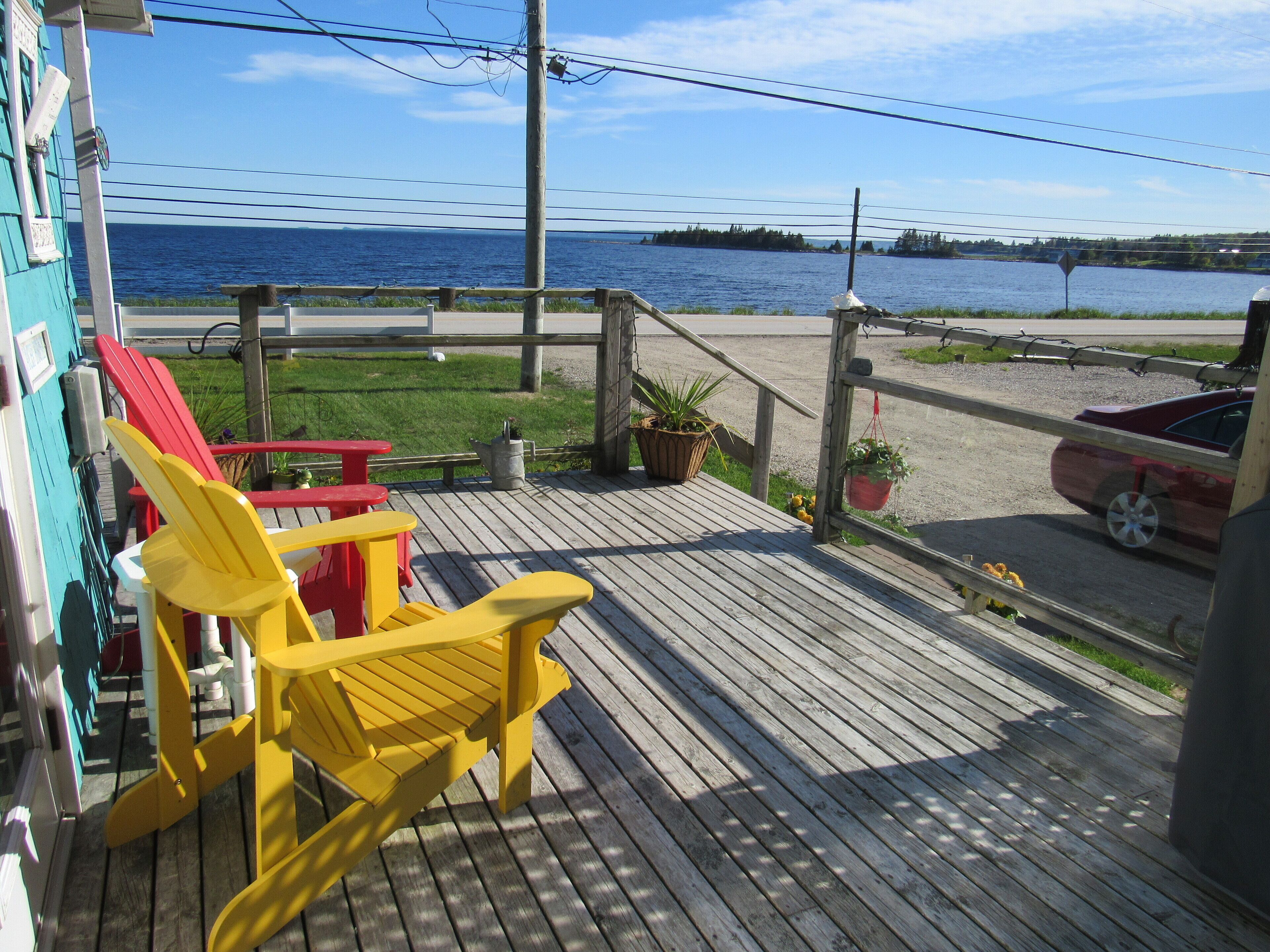 Une terrasse en bois agrémentée de chaises Adirondack aux couleurs vives, d’une petite table et de plantes en pot.